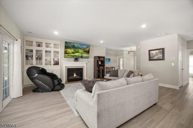 living area with light wood-style floors, a fireplace with flush hearth, visible vents, and recessed lighting