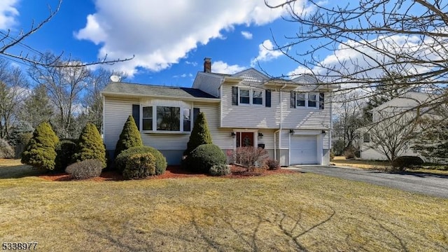 tri-level home with aphalt driveway, a chimney, a garage, and a front lawn