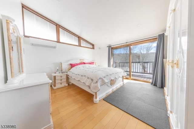 bedroom featuring access to exterior, light wood-style flooring, vaulted ceiling, and a wall mounted AC