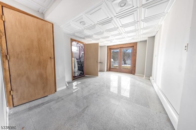 empty room featuring an ornate ceiling, baseboards, and french doors