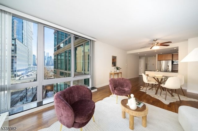 living room featuring a wall of windows, ceiling fan, and wood-type flooring