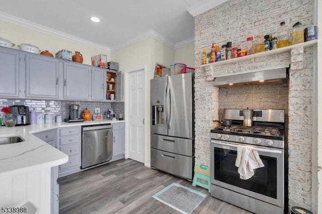 kitchen featuring light wood-type flooring, exhaust hood, stainless steel appliances, ornamental molding, and tasteful backsplash