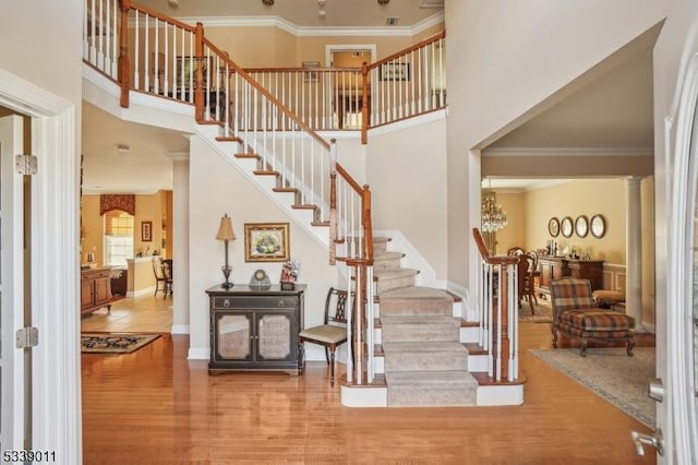 entryway with wood-type flooring, ornate columns, crown molding, and a high ceiling