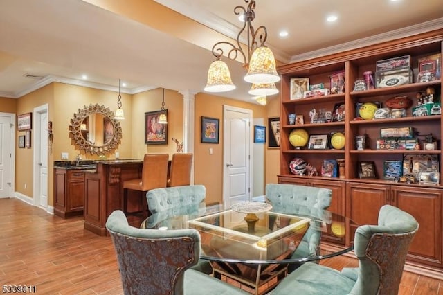 sitting room featuring sink, light wood-type flooring, crown molding, and ornate columns