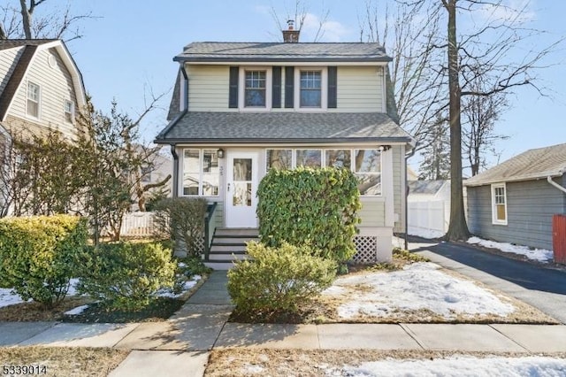 view of front facade with a shingled roof, entry steps, driveway, and a chimney