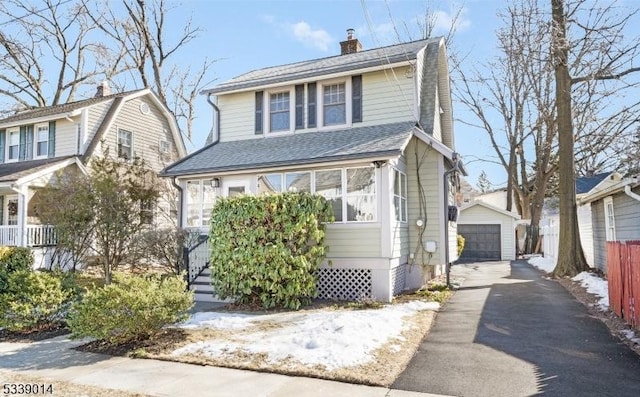 view of front of house with a detached garage, a chimney, aphalt driveway, fence, and an outdoor structure