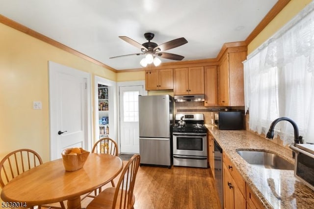 kitchen featuring dark wood finished floors, crown molding, stainless steel appliances, a sink, and under cabinet range hood