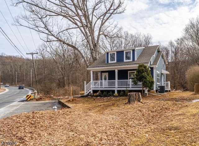 view of front of property with covered porch, a forest view, roof with shingles, and central air condition unit