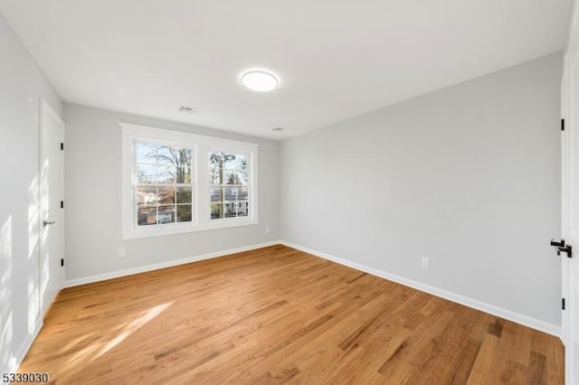 empty room with light wood finished floors, visible vents, and baseboards