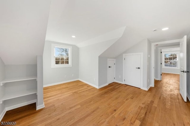 additional living space featuring vaulted ceiling, light wood-style flooring, a wealth of natural light, and baseboards