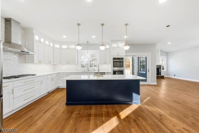 kitchen with light countertops, double oven, glass insert cabinets, a kitchen island, and wall chimney range hood