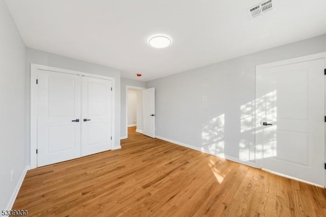 unfurnished bedroom featuring light wood-style flooring, a closet, visible vents, and baseboards