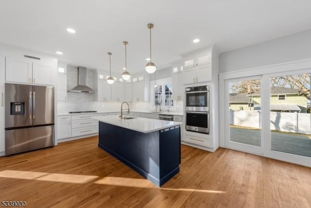 kitchen with a sink, white cabinets, light countertops, appliances with stainless steel finishes, and wall chimney exhaust hood