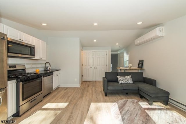 kitchen with stainless steel appliances, an AC wall unit, sink, white cabinetry, and a baseboard heating unit