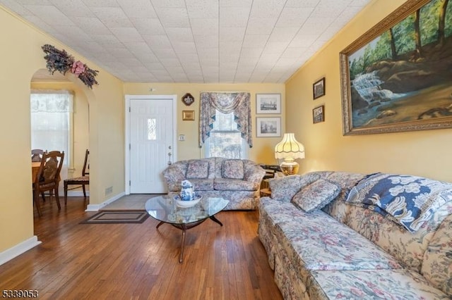 living room featuring arched walkways, baseboards, and hardwood / wood-style flooring