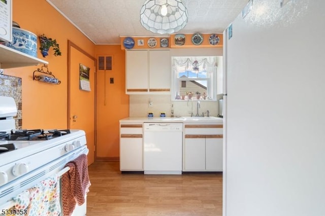 kitchen with light countertops, visible vents, white cabinets, a sink, and white appliances