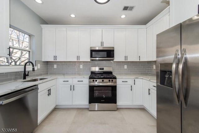 kitchen with appliances with stainless steel finishes, light stone countertops, decorative backsplash, sink, and white cabinetry