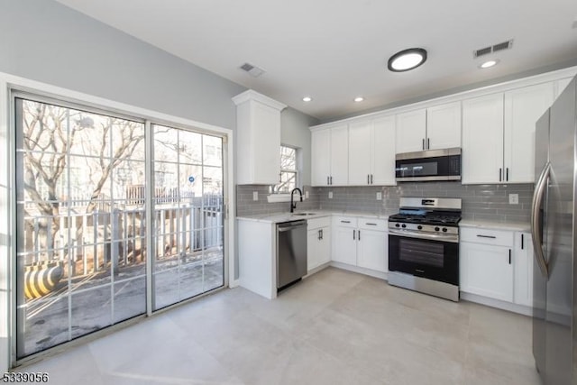 kitchen with appliances with stainless steel finishes, light stone counters, decorative backsplash, sink, and white cabinetry