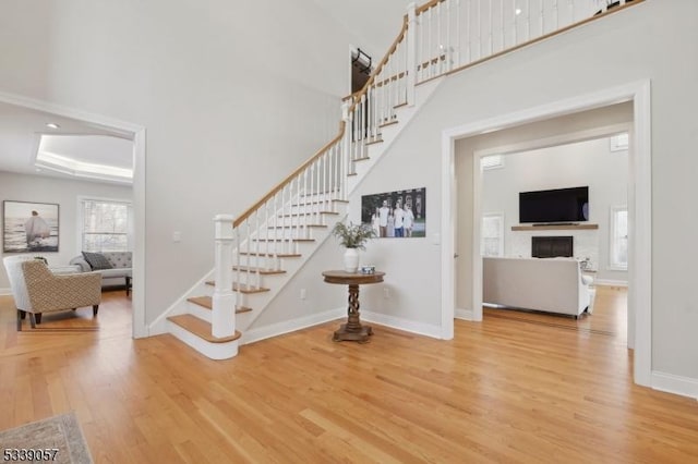 stairway featuring a fireplace, wood finished floors, a towering ceiling, baseboards, and a raised ceiling