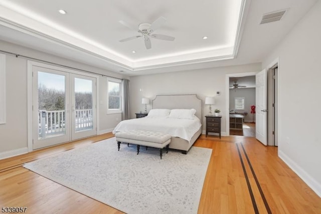 bedroom with access to exterior, a tray ceiling, light wood-type flooring, and visible vents