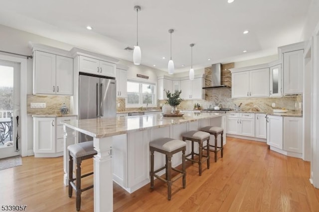 kitchen with a breakfast bar, white cabinets, a kitchen island, high quality fridge, and wall chimney range hood