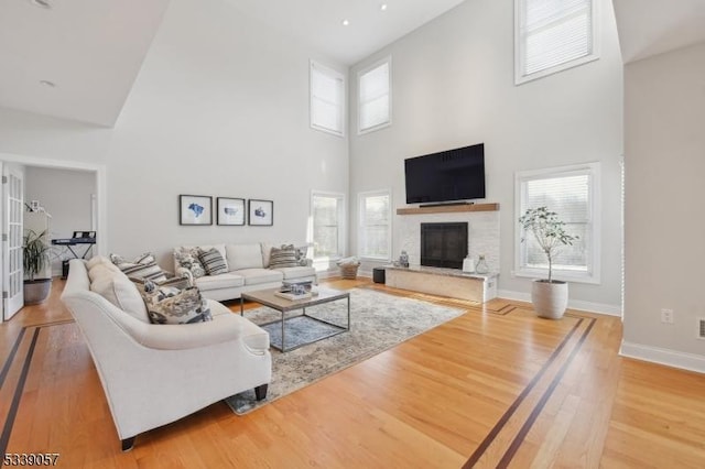 living area featuring a glass covered fireplace, wood finished floors, a high ceiling, and baseboards