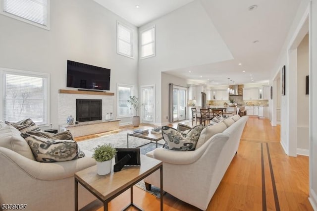 living area featuring recessed lighting, a high ceiling, light wood-style floors, a glass covered fireplace, and baseboards