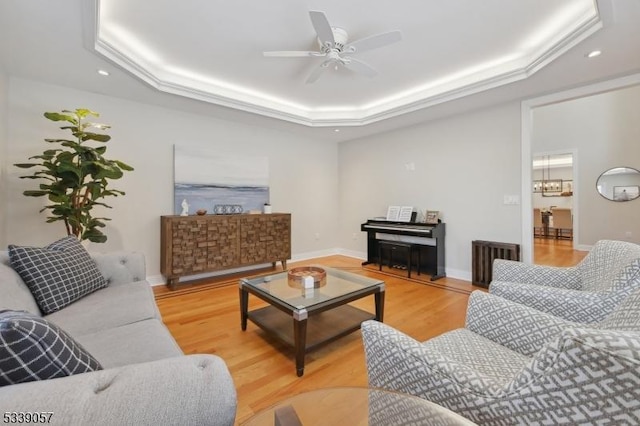 living room featuring a tray ceiling, ceiling fan, baseboards, and wood finished floors