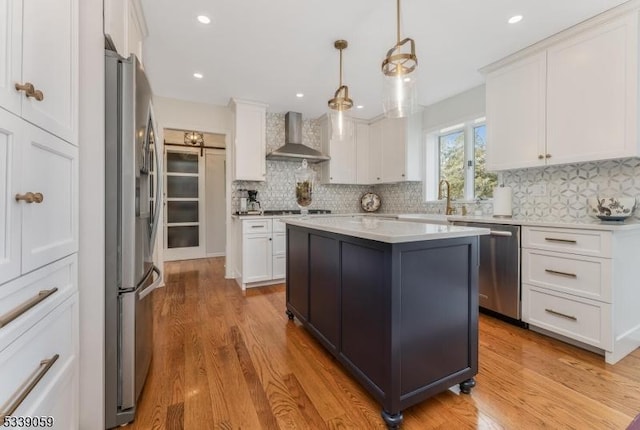 kitchen featuring a center island, stainless steel appliances, light countertops, wall chimney range hood, and white cabinetry