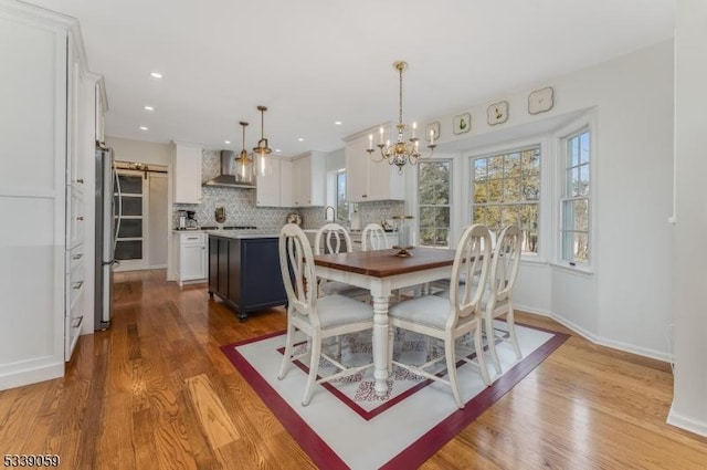 dining area with recessed lighting, an inviting chandelier, light wood-style floors, a barn door, and baseboards