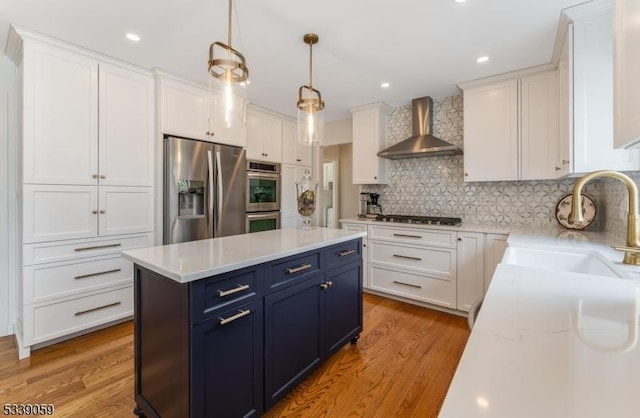 kitchen featuring stainless steel appliances, white cabinetry, a sink, wall chimney range hood, and blue cabinets