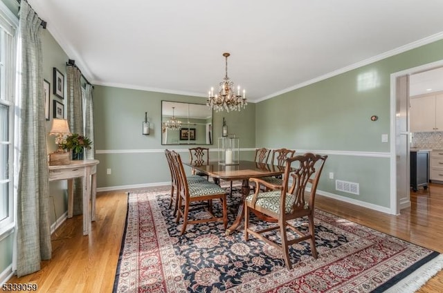 dining room with a chandelier, light wood-style flooring, visible vents, and crown molding