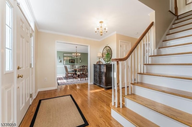 entryway with a chandelier, wood finished floors, baseboards, ornamental molding, and stairway