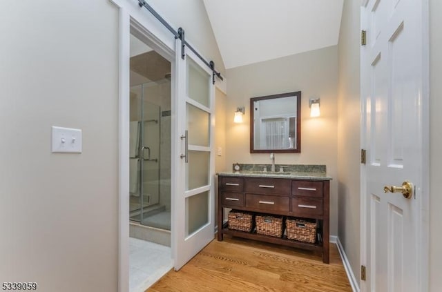 bathroom with a stall shower, baseboards, wood finished floors, vaulted ceiling, and vanity