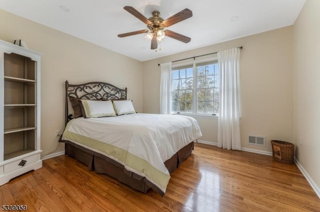 bedroom with light wood-style floors, visible vents, baseboards, and a ceiling fan