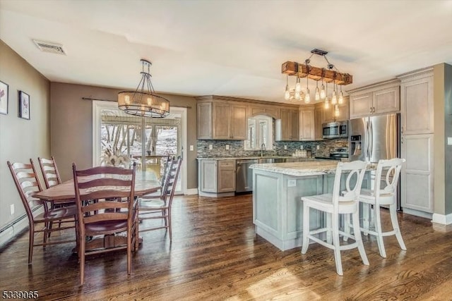 kitchen featuring appliances with stainless steel finishes, hanging light fixtures, backsplash, a kitchen island, and dark hardwood / wood-style floors