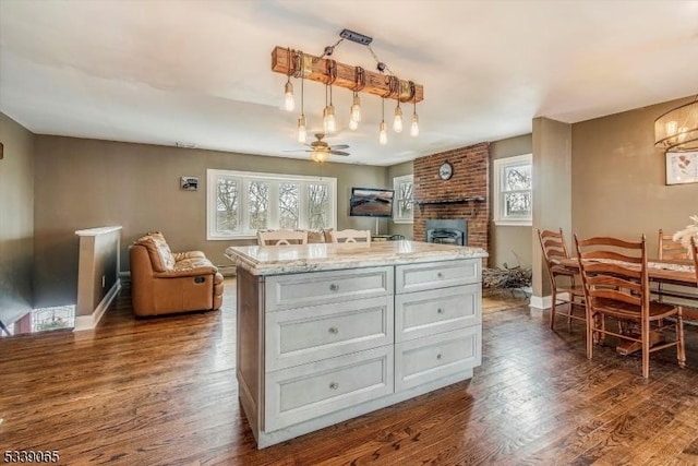 kitchen with light stone counters, white cabinets, ceiling fan, a center island, and dark hardwood / wood-style flooring