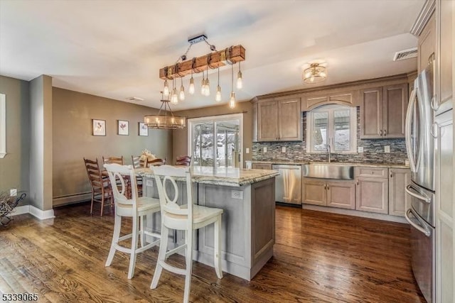 kitchen with hanging light fixtures, stainless steel appliances, light stone counters, a kitchen island, and sink