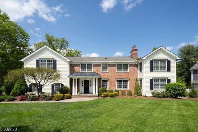 view of front of home featuring brick siding, a chimney, and a front yard