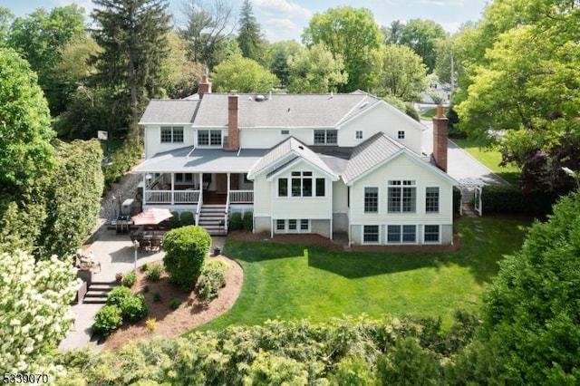 rear view of property featuring stairs, a chimney, a patio area, and a lawn