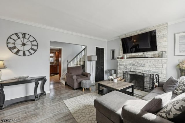 living area featuring a stone fireplace, wood finished floors, baseboards, ornamental molding, and stairway