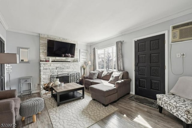 living area with a wall unit AC, a fireplace, wood finished floors, baseboards, and ornamental molding