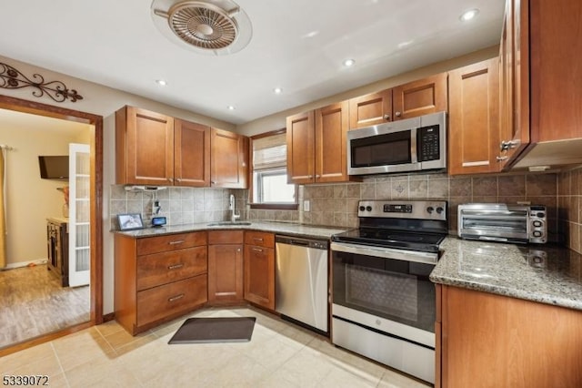 kitchen featuring light stone counters, a sink, appliances with stainless steel finishes, tasteful backsplash, and brown cabinetry