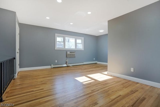 empty room with baseboard heating, light hardwood / wood-style flooring, and a wall mounted AC