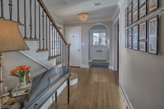 entrance foyer featuring baseboards, arched walkways, crown molding, and wood finished floors