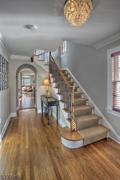 stairway with arched walkways, ornamental molding, wood finished floors, and baseboards