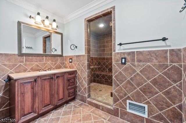 bathroom with a shower with door, tile patterned flooring, ornamental molding, tile walls, and vanity