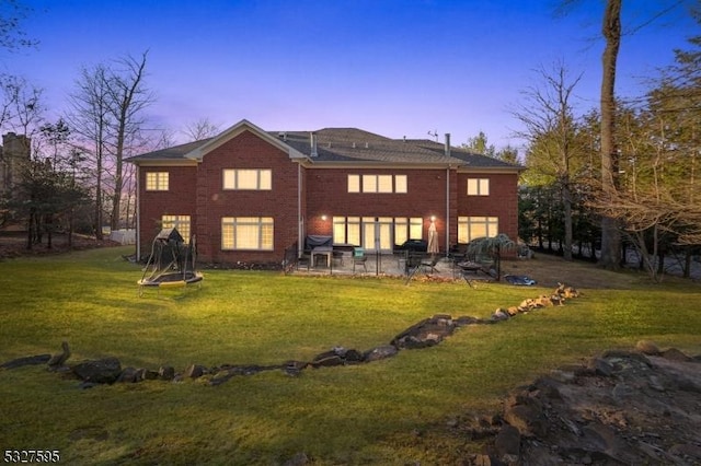 back house at dusk with a lawn and a patio