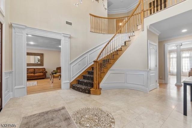 stairs with a high ceiling, crown molding, and decorative columns