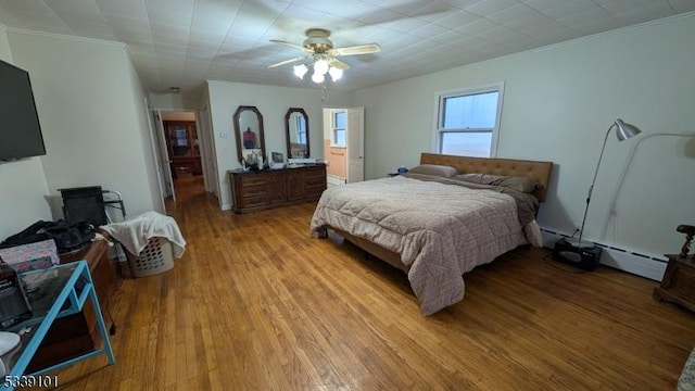 bedroom with light wood-type flooring, crown molding, and a baseboard heating unit